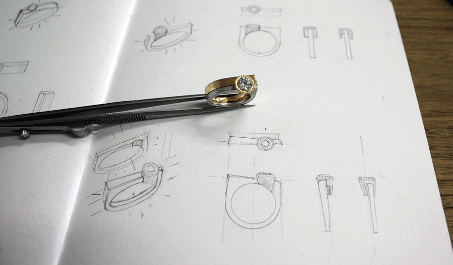 Engagement and wedding ring set held by tweezers over the original pencil drawings for the design.