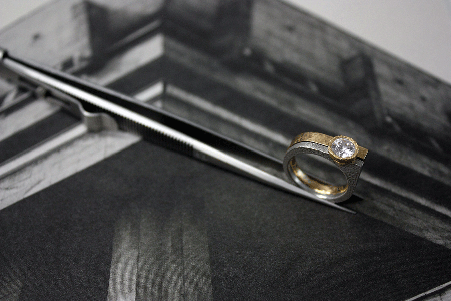 Engagement and wedding ring set held by tweezers over a photo of brutalist architecture.