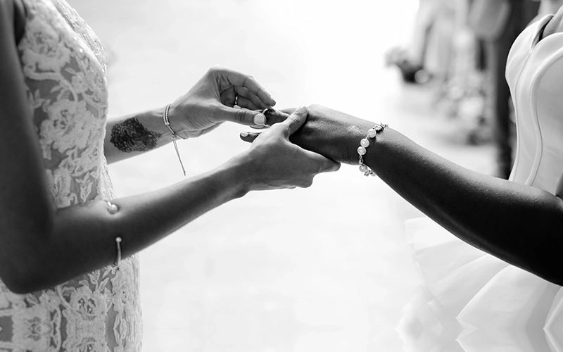 the arms and hands of one woman placing a wedding ring on the hand of another