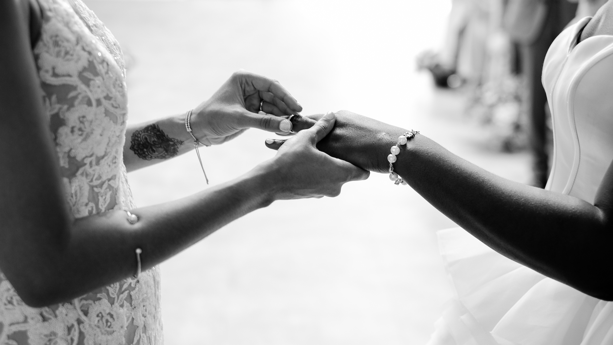 the arms and hands of one woman placing a wedding ring on the hand of another