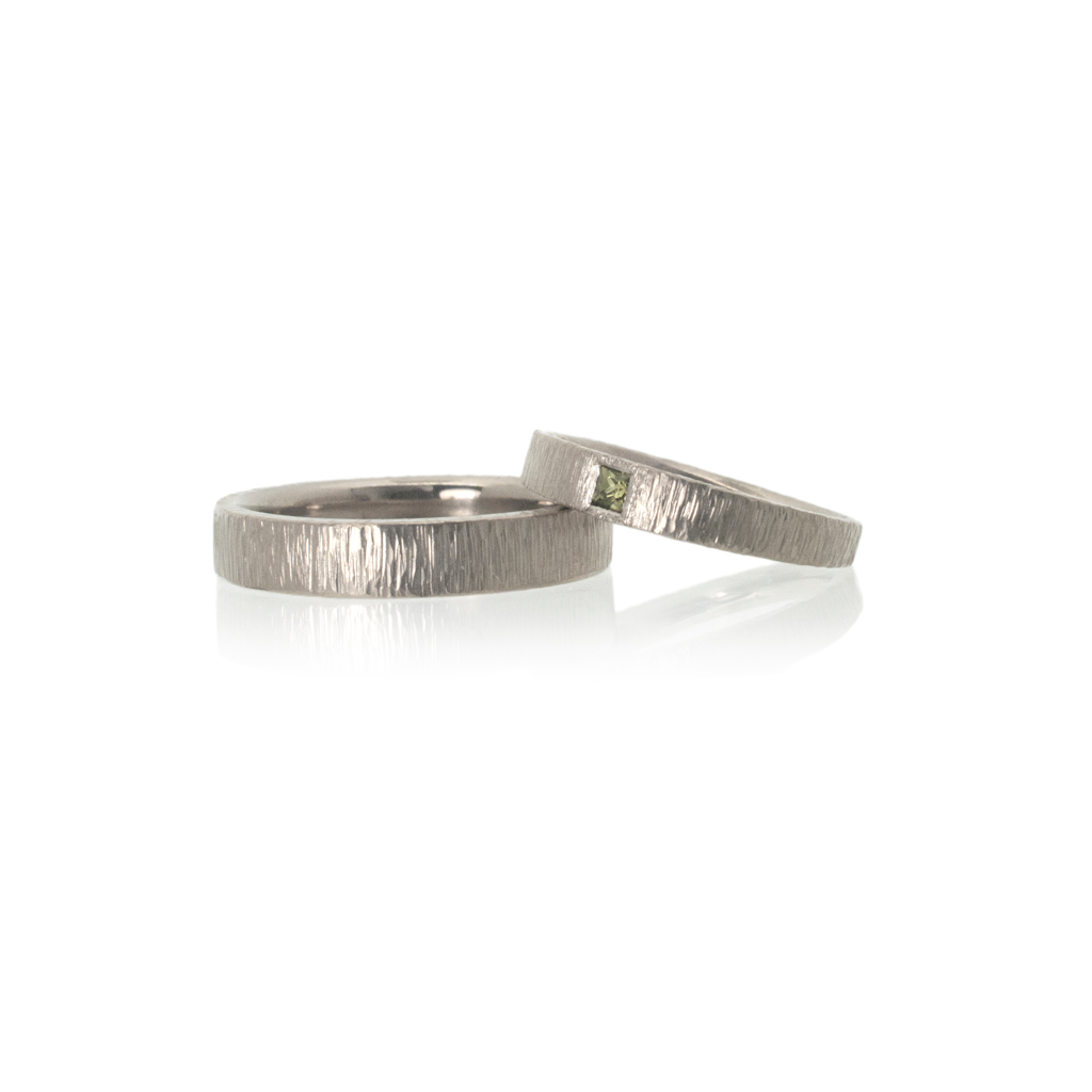 Women's wedding ring laying on a men's wedding ring on a white background