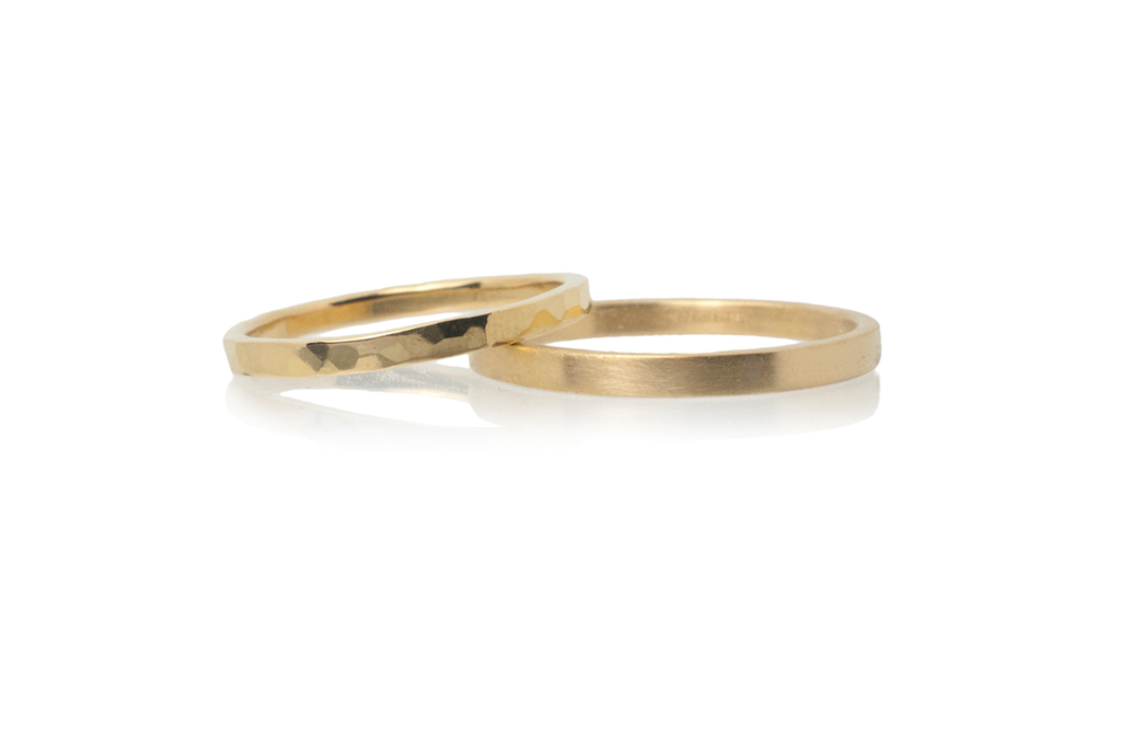 A pair of narrow yellow gold wedding rings with hammered and matte finishes on a white background.