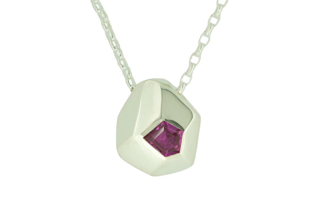 Contemporary silver pendant set with freeform ruby hanging on a white background.