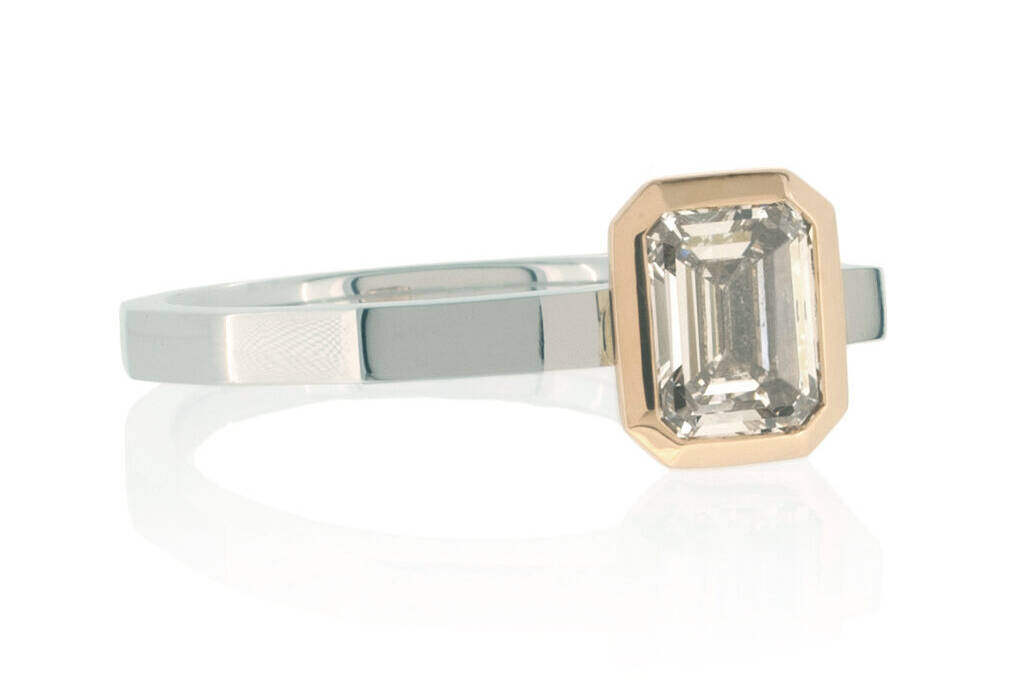 Emerald cut diamond ring in platinum and rose gold on a white background.