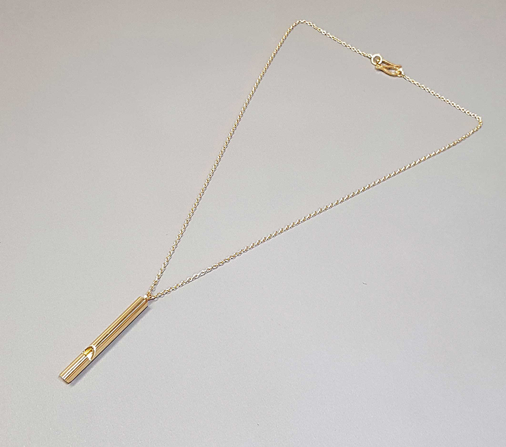 Gold whistle necklace flat lay on grey background/