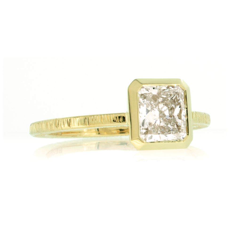 Radiant cut diamond solitaire ring in yellow gold on a white background.