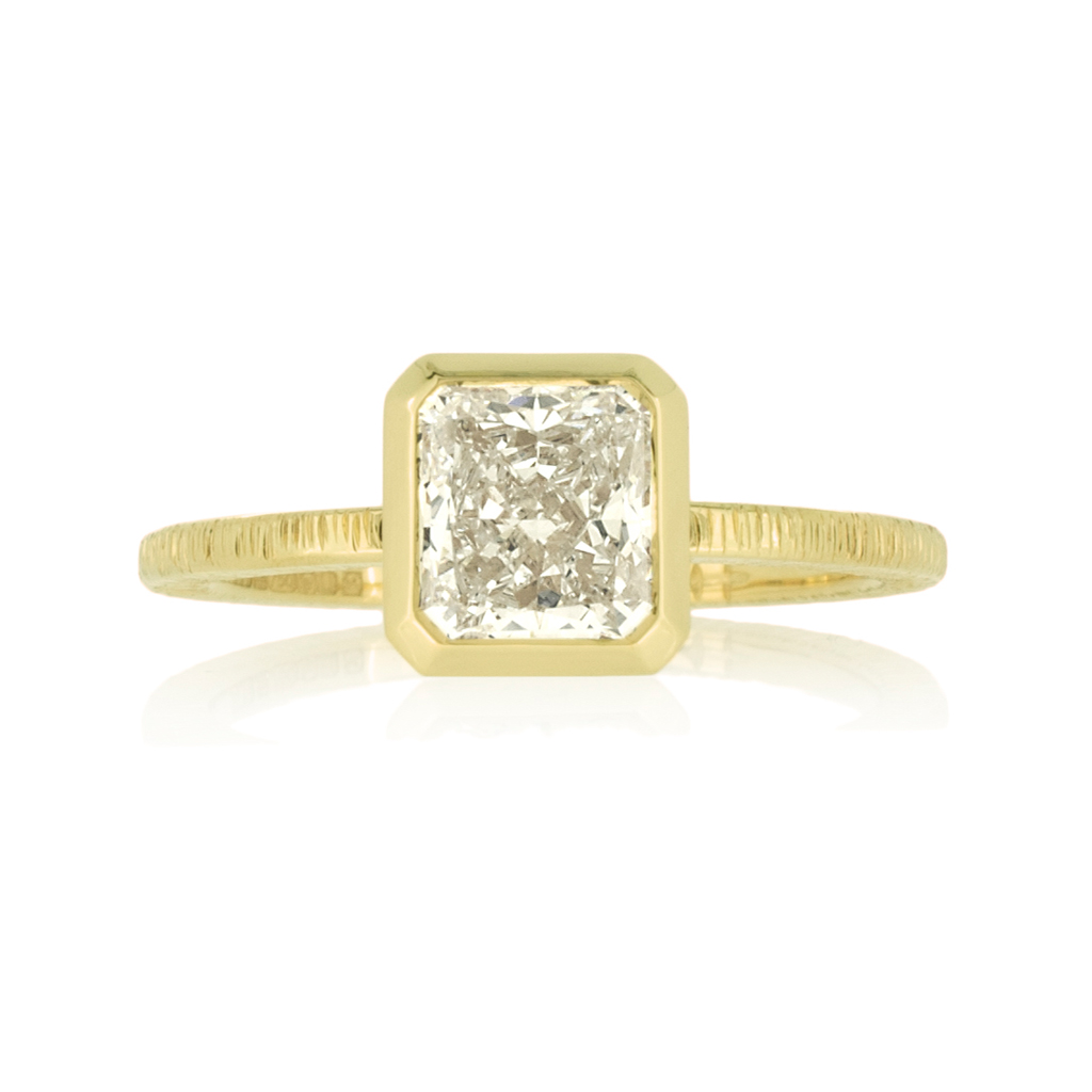 Radiant cut diamond solitaire ring in yellow gold on a white background.