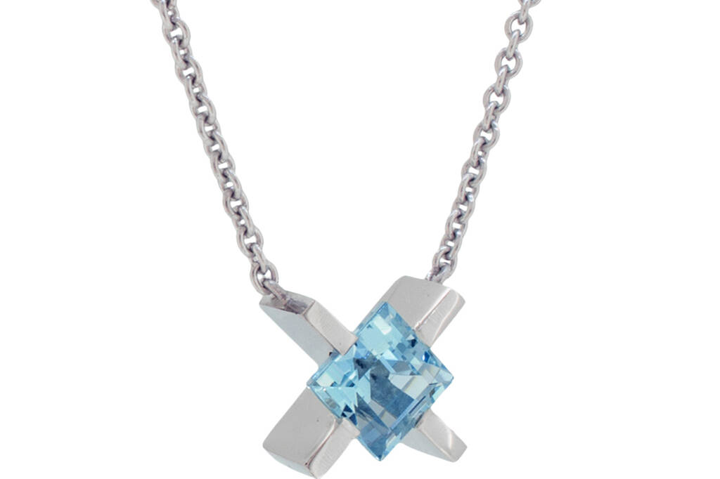 Platinum 'X' pendant with a square cut aquamarine hanging on a chain in front of a white background.