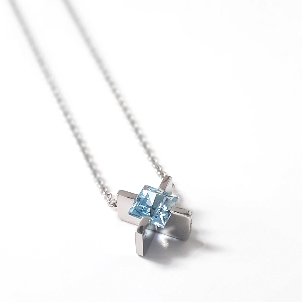 platinum X shaped pendant set with a square aquamarine stone, lying on a white background