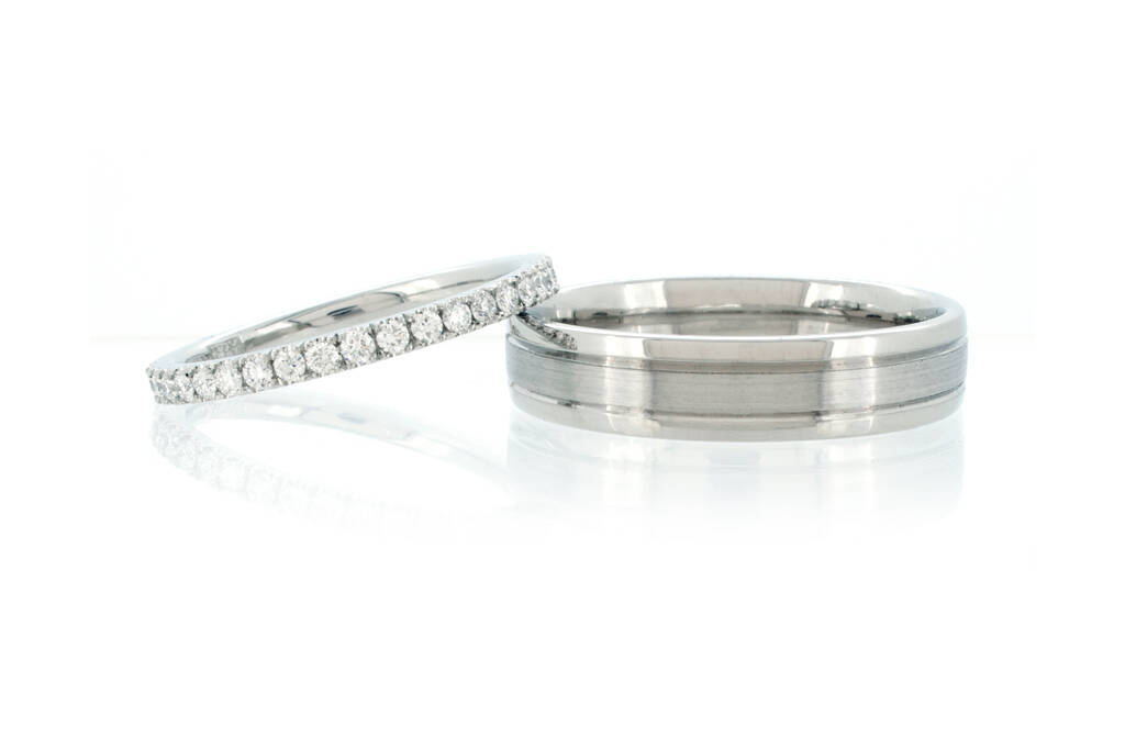 Diamond eternity ring and men's wedding ring with two groove set against a white background.