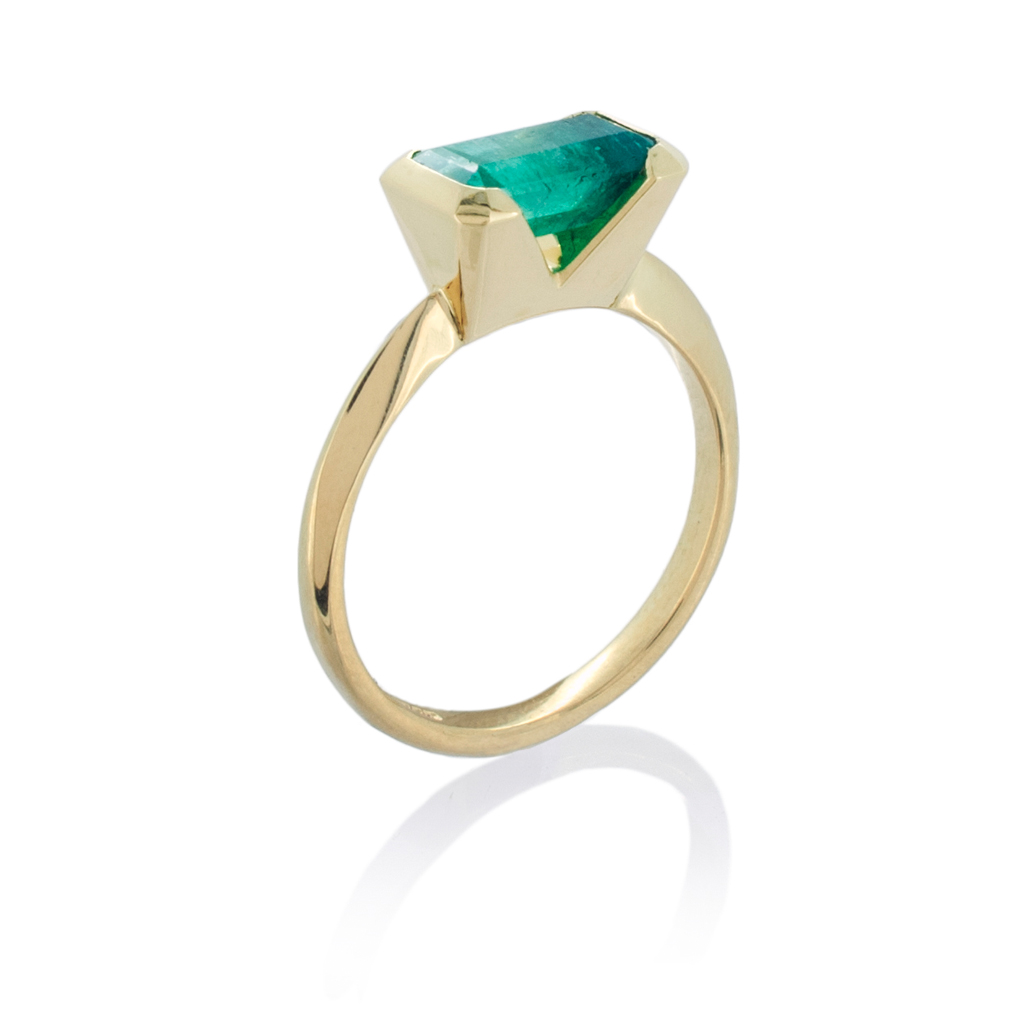 art deco style engagement ring with a single square emerald on a yellow gold band, on a white background