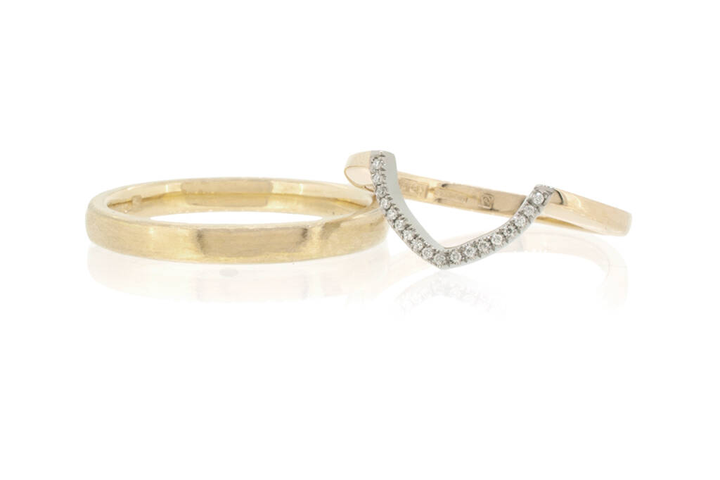 Woman's Fairtrade Gold wishbone ring set with diamonds resting on a man's courtshaped band. Both rings are set against a white background.