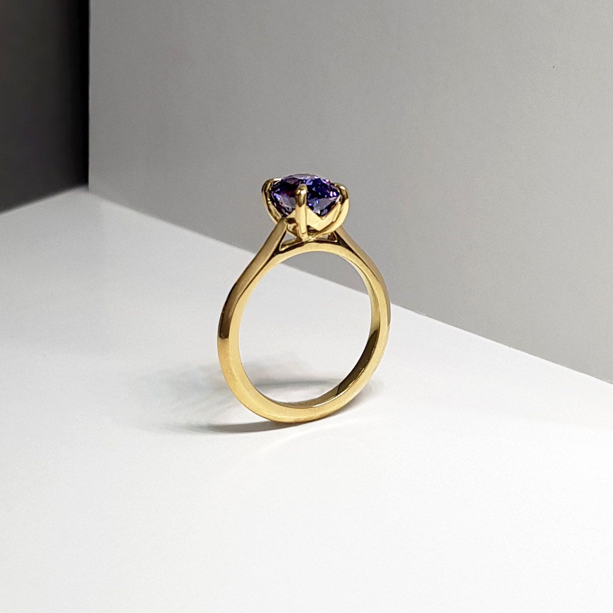 a single stone natural purple sapphire and gold engagement ring, standing upright on a white background