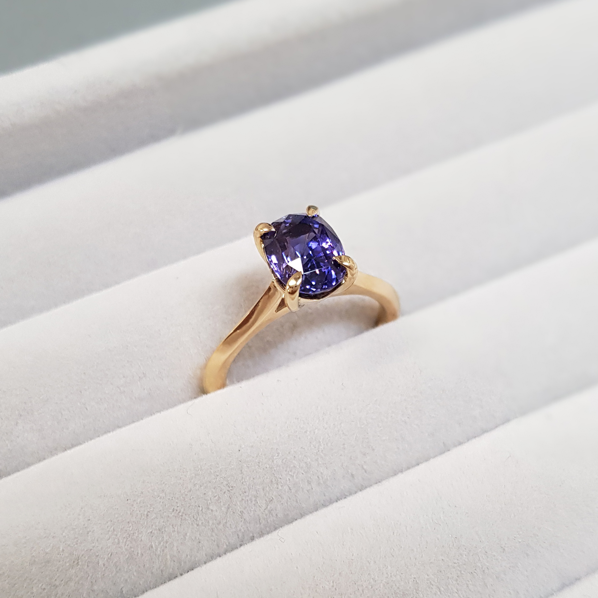 solitaire purple sapphire ring with a yellow gold band on a grey fabric background