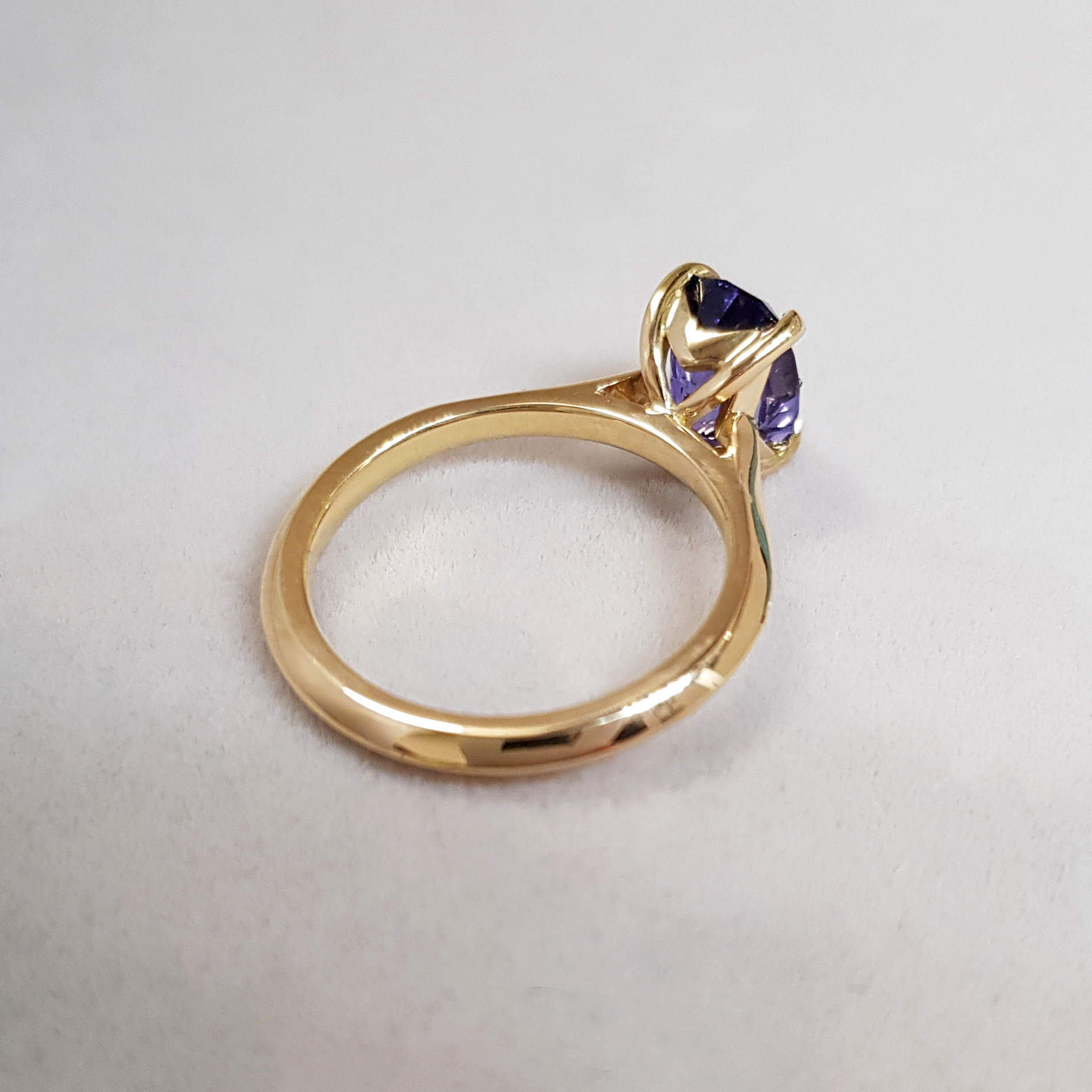 a yellow gold engagement ring, showing the underside of the setting holing a single purple sapphire stone
