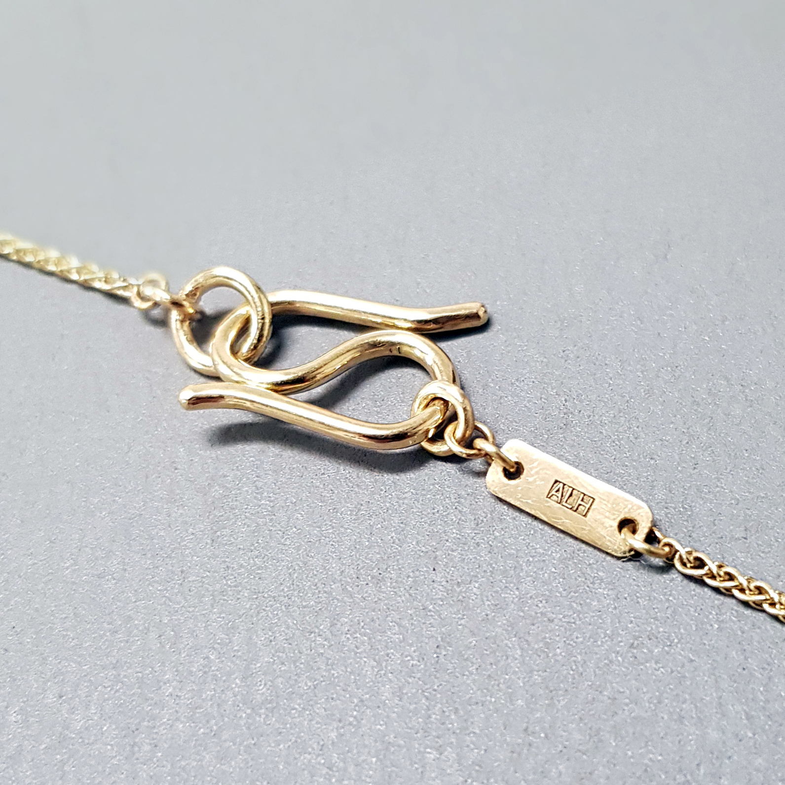 Handmade S clasp in 18k yellow gold with spiga chain on a grey background.