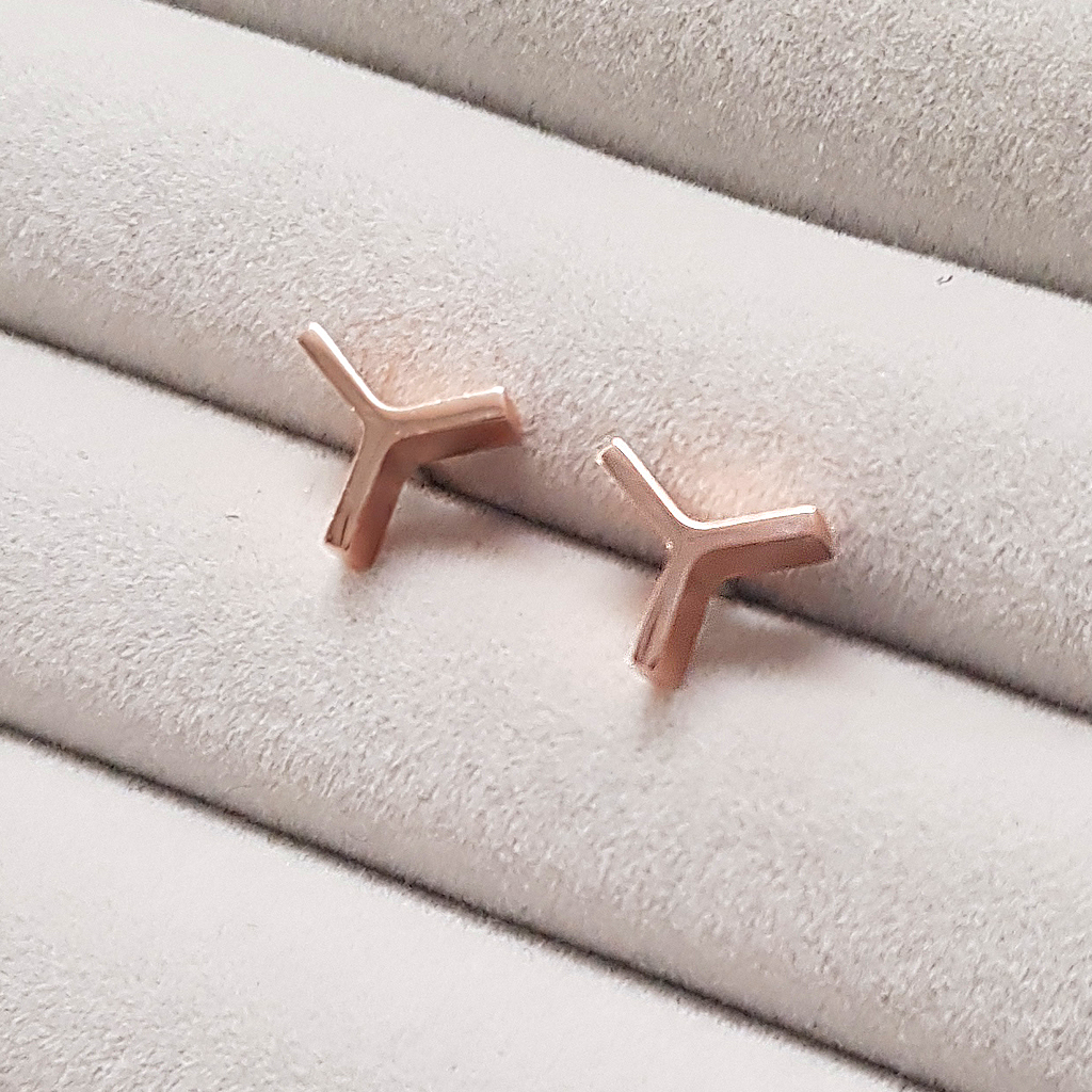 a pair of rose gold Y shaped stud earrings on a grey fabric background