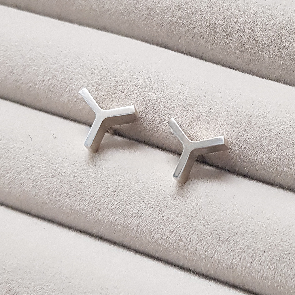 a pair of solid silver Y shaped stud earrings on a grey fabric background