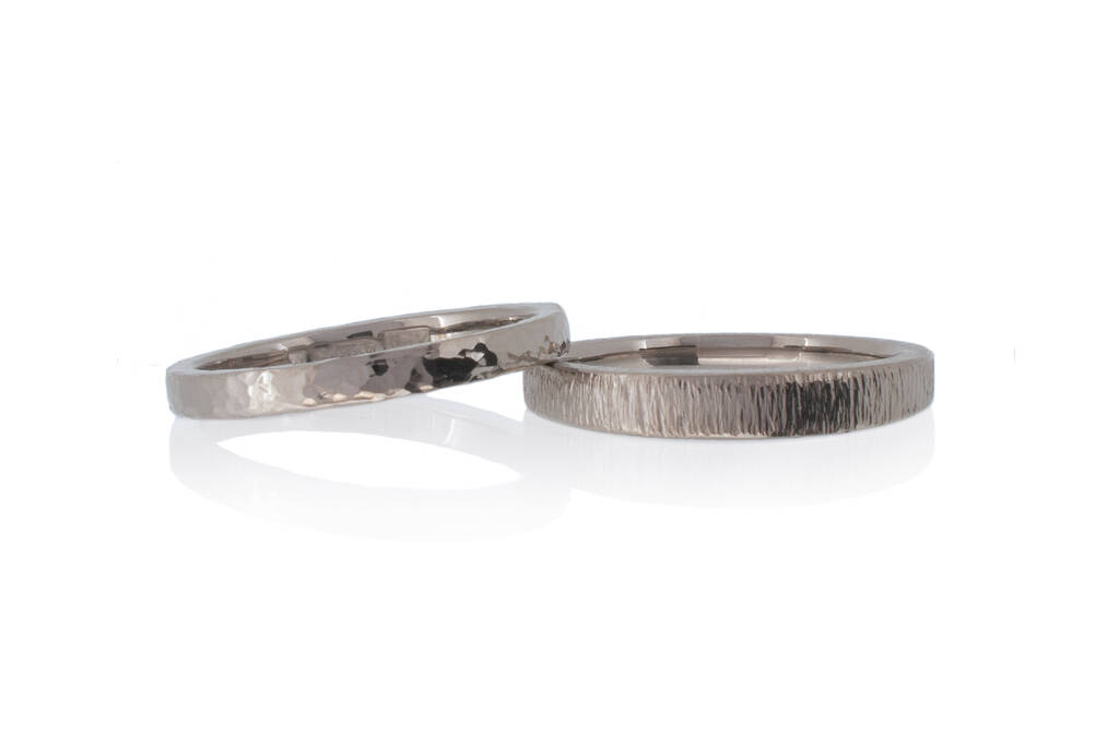Two narrow and textured (hammered) wedding rings, one resting on another against a white background.