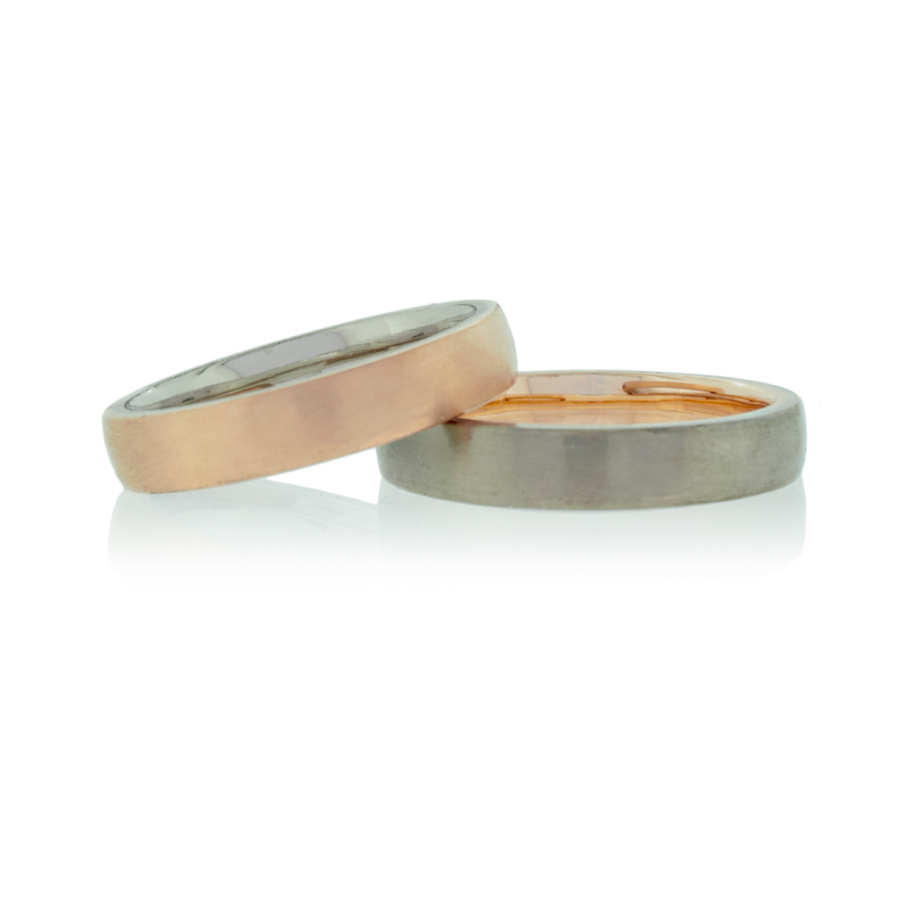 Two wedding rings in rose and white gold with one lying on the other on a white background.
