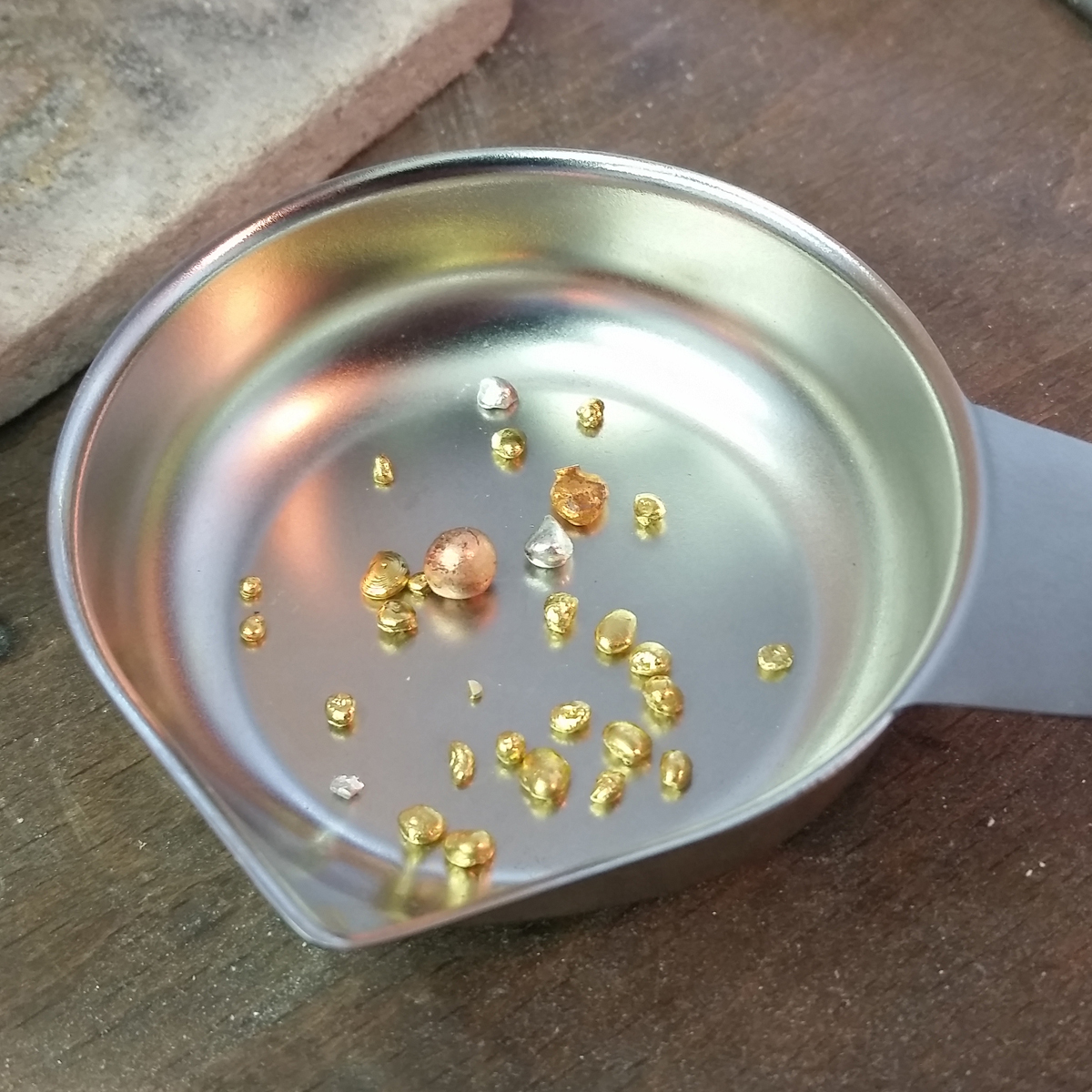 Grains of copper, silver and Fairtrade gold in a small weighing dish on a workbench.