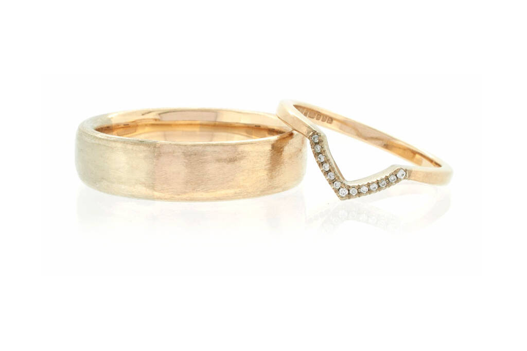Woman's wedding ring with a V-shaped detail set with diamonds resting on a man's ring. Both rings are set against a white background.