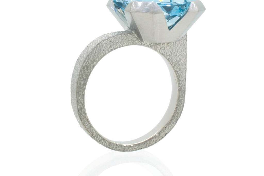 Aquamarine ring with offset stone standing upright on a white background.