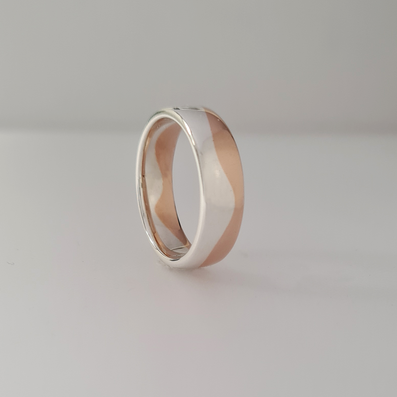 A wedding band with a wave design of contrasting rose and white gold on a white background