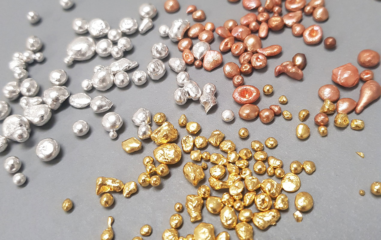 Scattered grains of pure gold, silver and copper on a grey background.