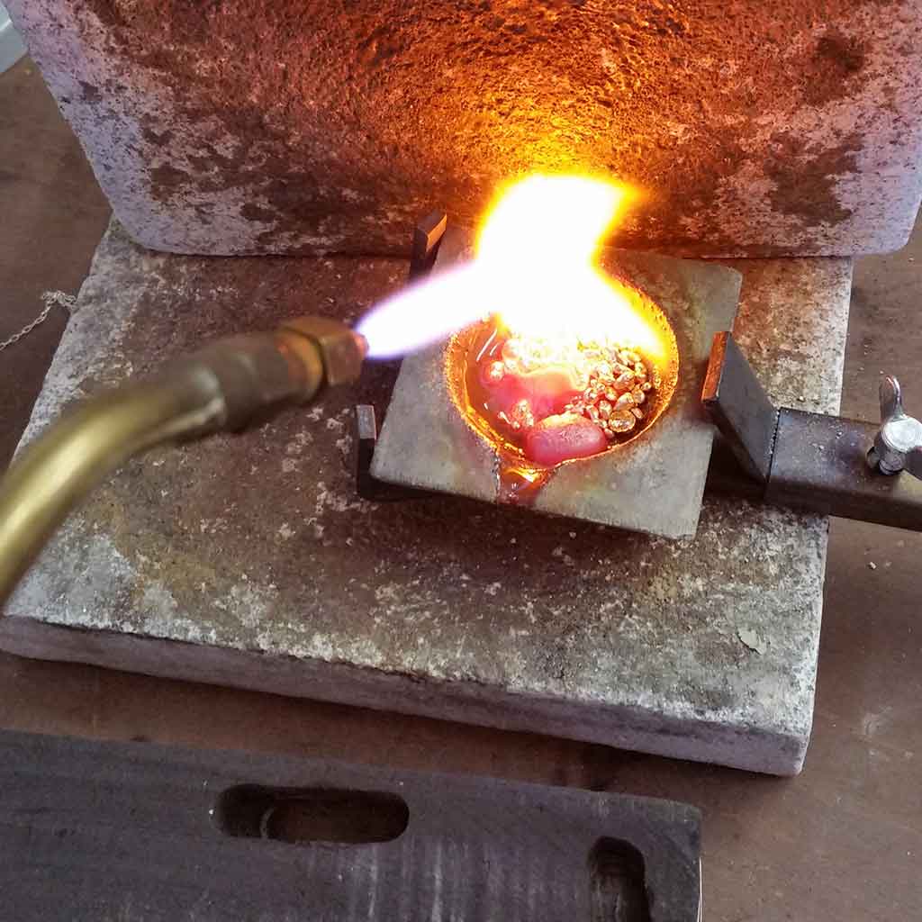 Lit torch melting pure gold, silver and copper in a scorfier.