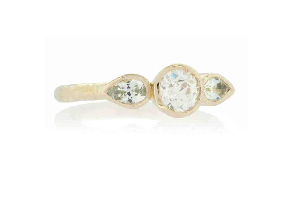Three stone ring with round diamond and two pear cut topaz in yellow gold on white background.