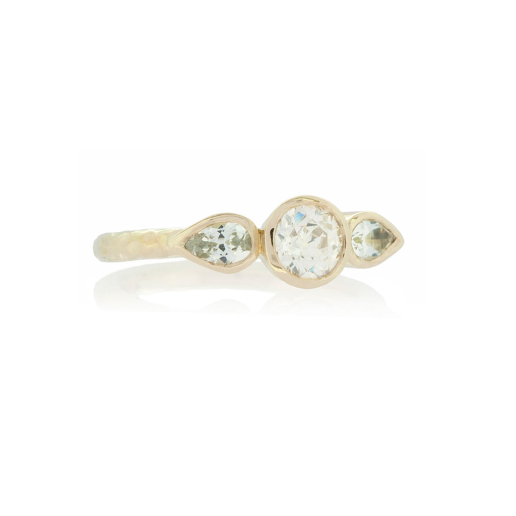 Three stone ring with round diamond and two pear cut topaz in yellow gold on white background.