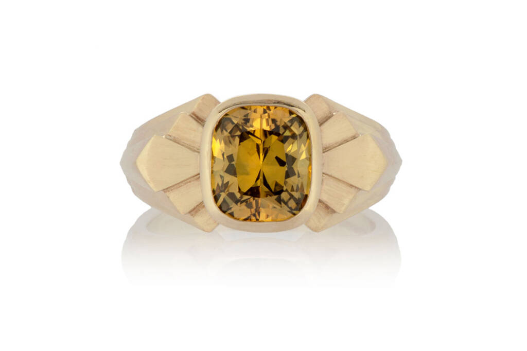 a gold signet ring with art deco design with a large yellow sapphire in the centre, on a white background