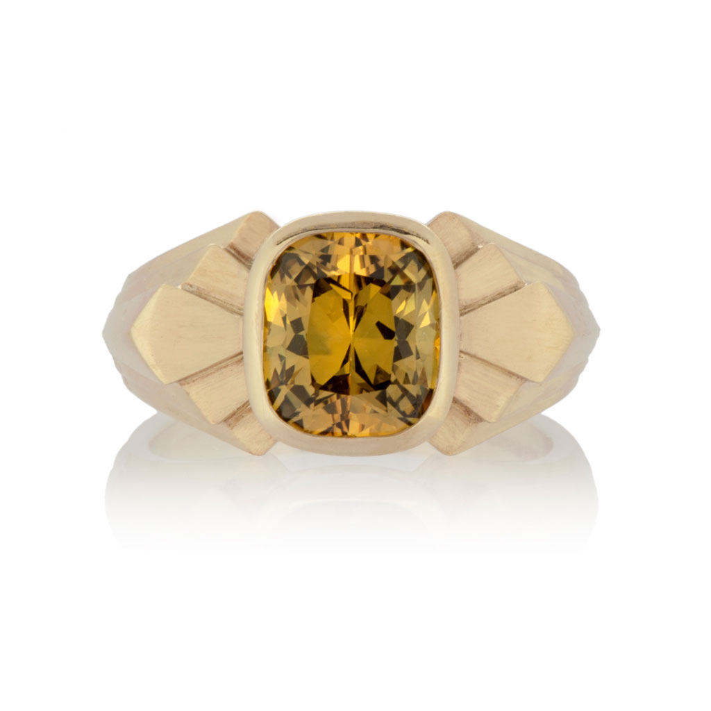 a gold signet ring with art deco design with a large yellow sapphire in the centre, on a white background
