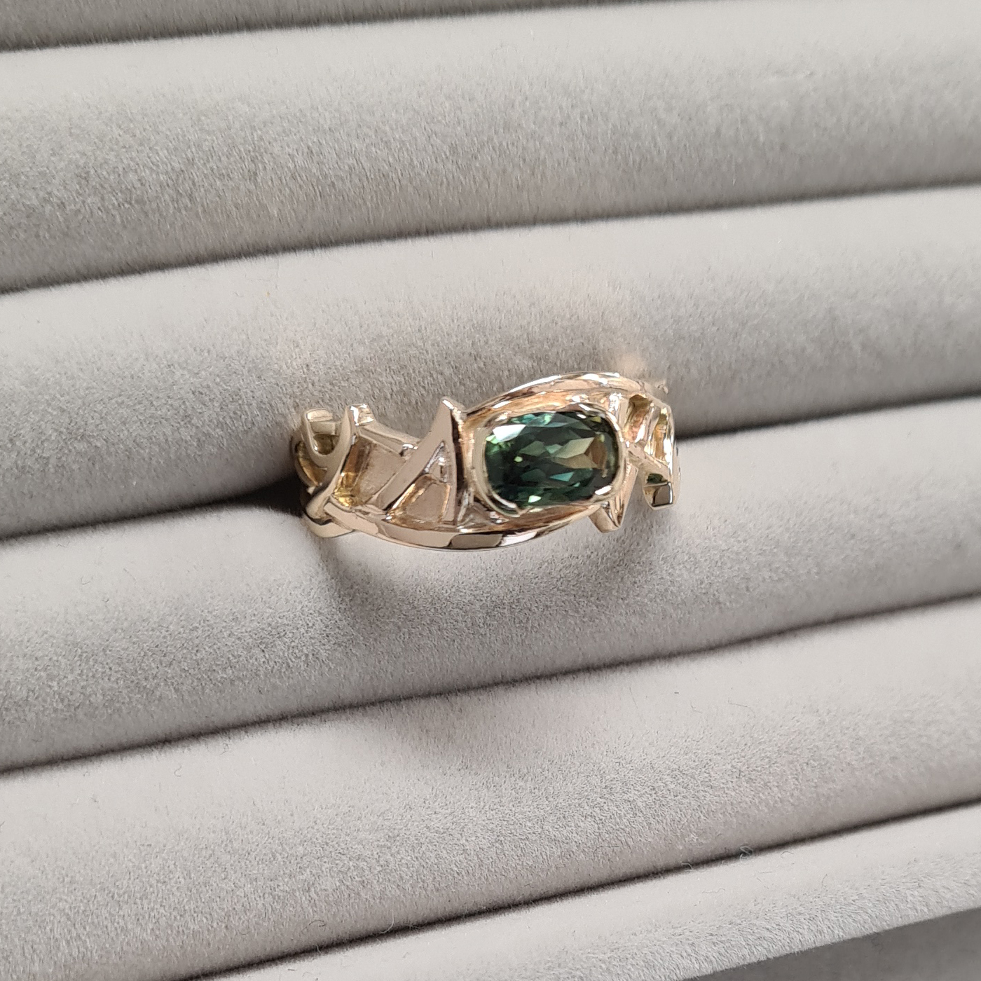 gold art nouveau ring with sculptural design of interweaving lines with a central blue-green sapphire, on a grey background