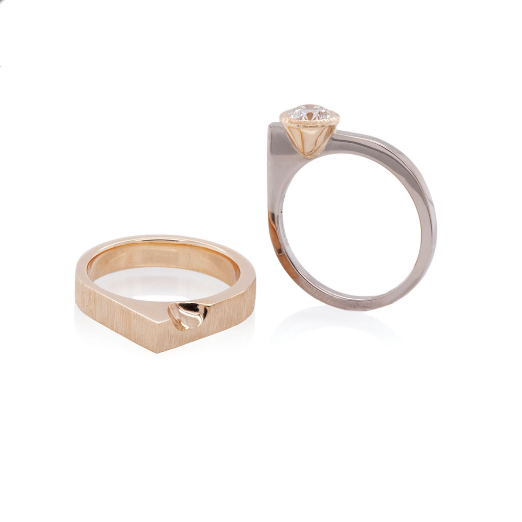 White gold engagement ring with one square corner sitting upright next to another in yellow gold
