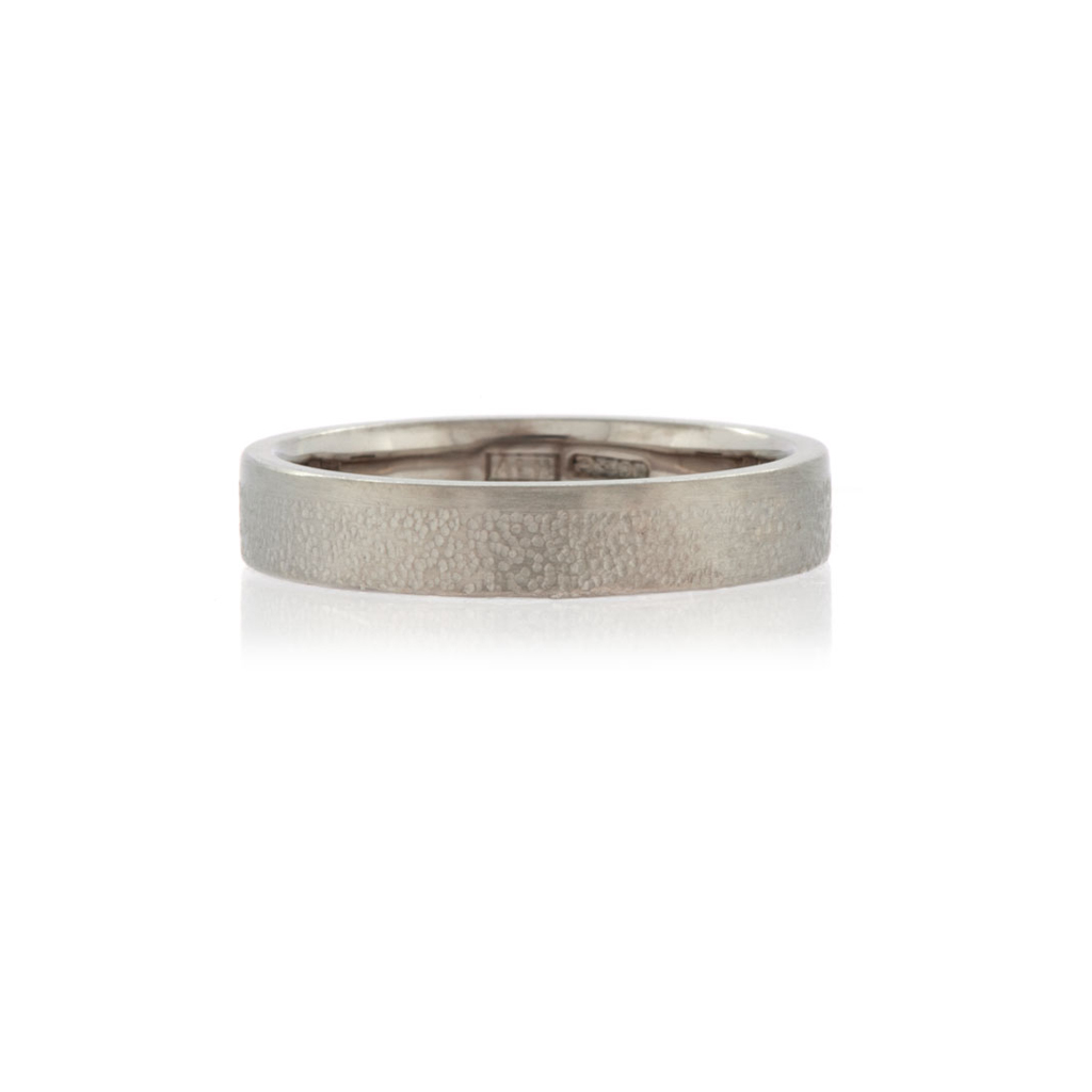 a white gold wedding band with a textured finish on a white background