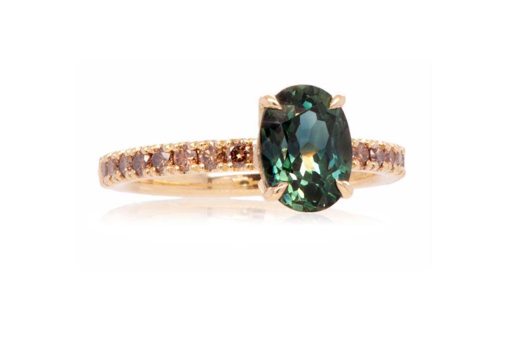 Engagement ring with a central teal sapphire and champagne diamonds on a gold band against a white background