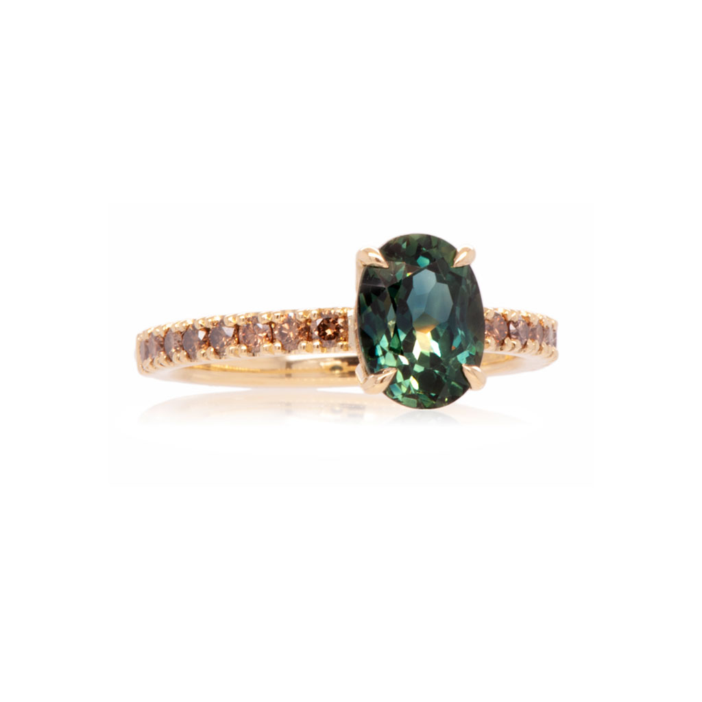 Engagement ring with a central teal sapphire and champagne diamonds on a gold band against a white background