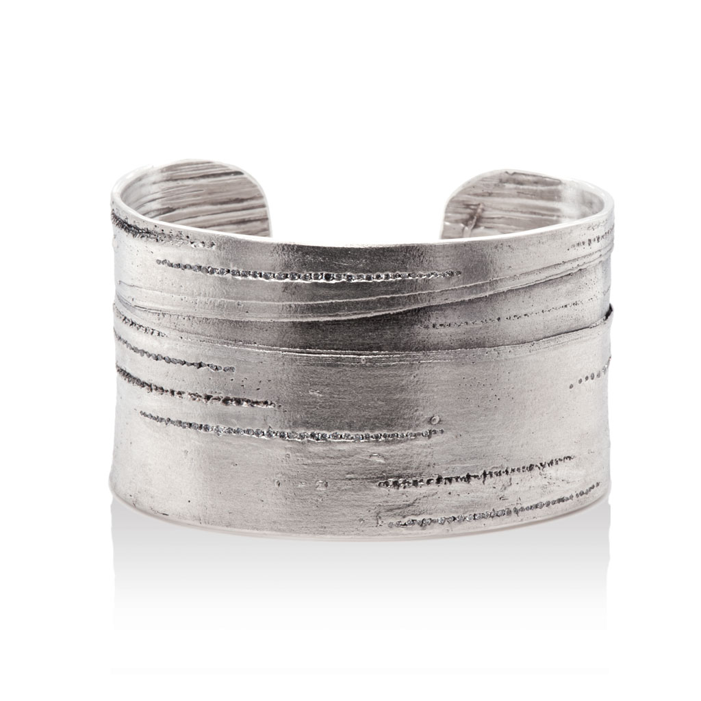 Silver cuff bracelet with lined texture of silver birch embedded with diamonds against a white background.