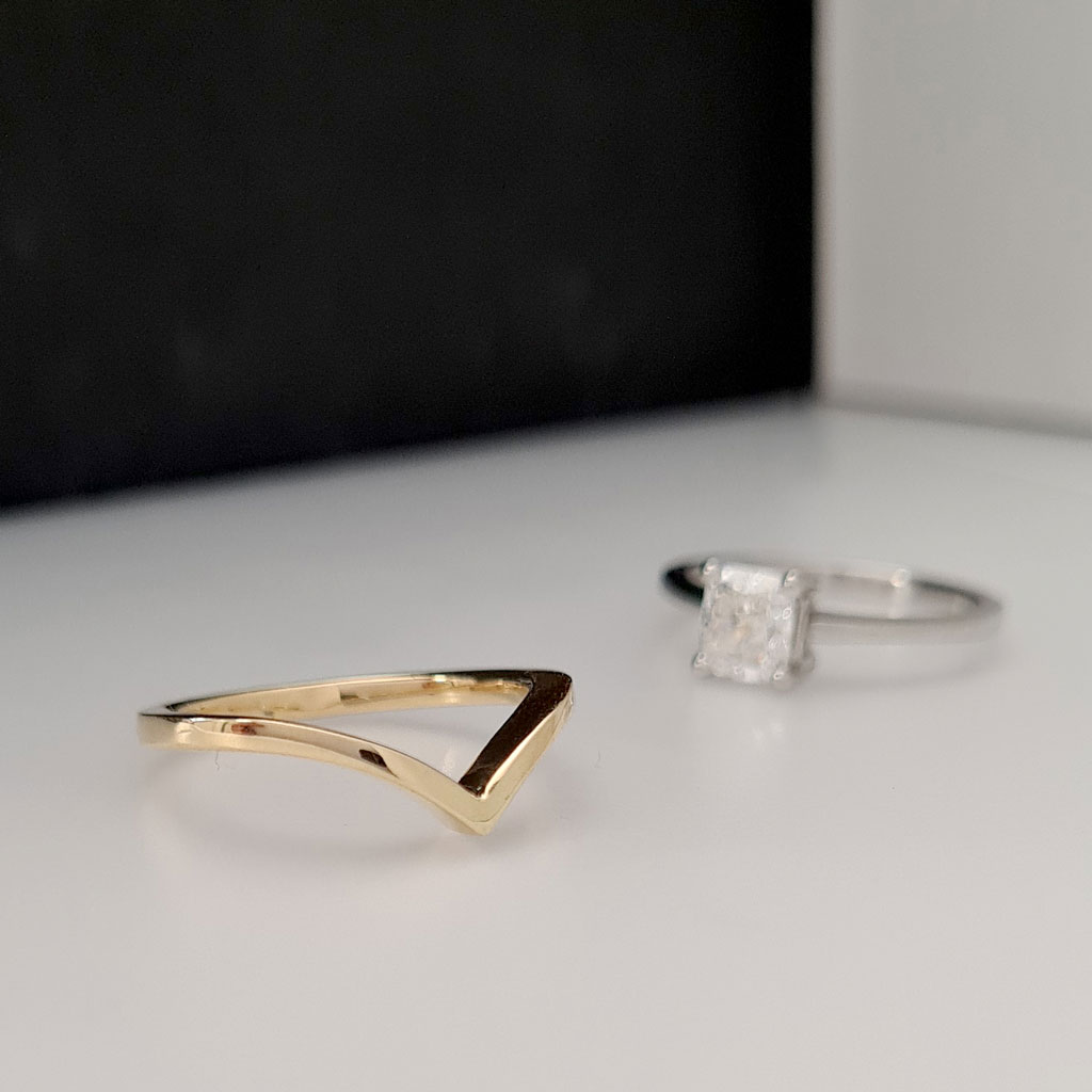 Tapered wishbone wedding ring and the bride's own solitaire engagement ring on a white, grey and black colour block background.