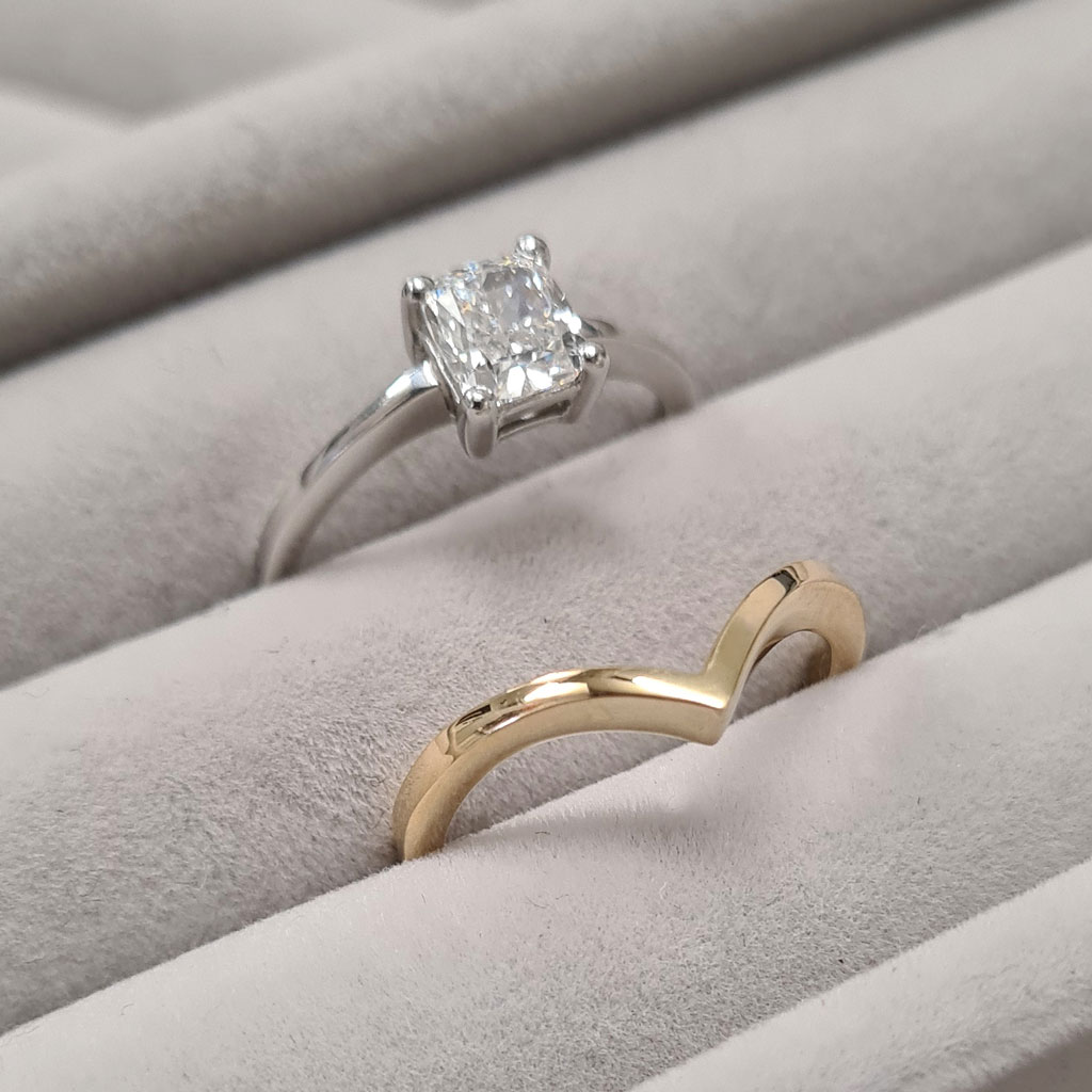 Delicate and tapered wishbone wedding ring on a gray velvet tray with the bride's own solitaire diamond engagement ring.