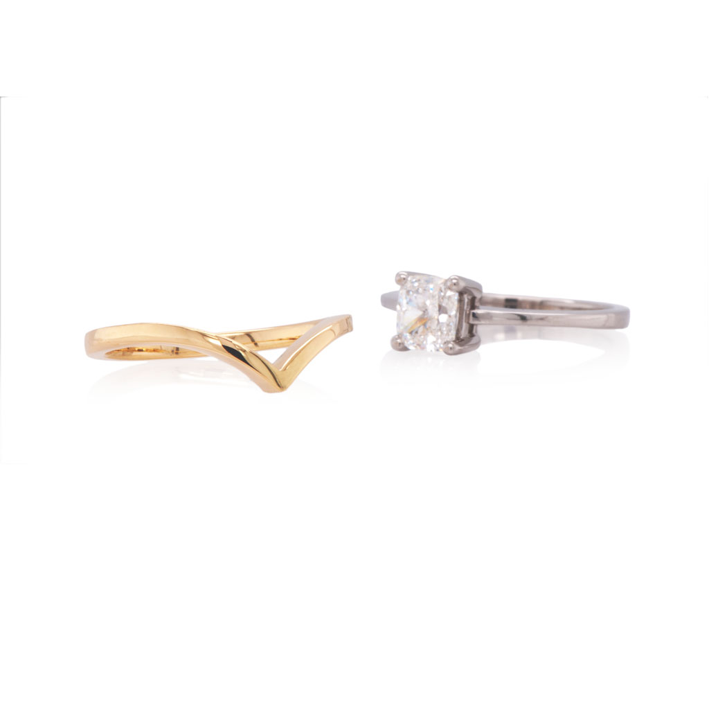 Delicate wishbone wedding band in yellow gold with bride's own solitaire diamond engagement ring on a white background.