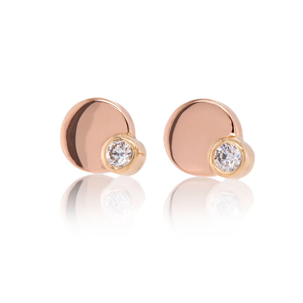 Diamond earring studs of an 8mm rose gold circle with a smaller diamond in yellow gold on the bottom right edge of each earring on a white background.