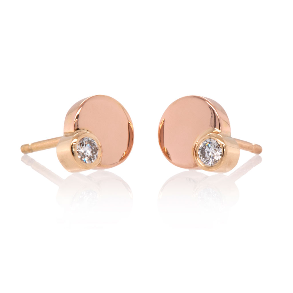 Diamond earring studs of an 8mm rose gold circle with a smaller diamond in yellow gold on the bottom edge of each earring on a white background.