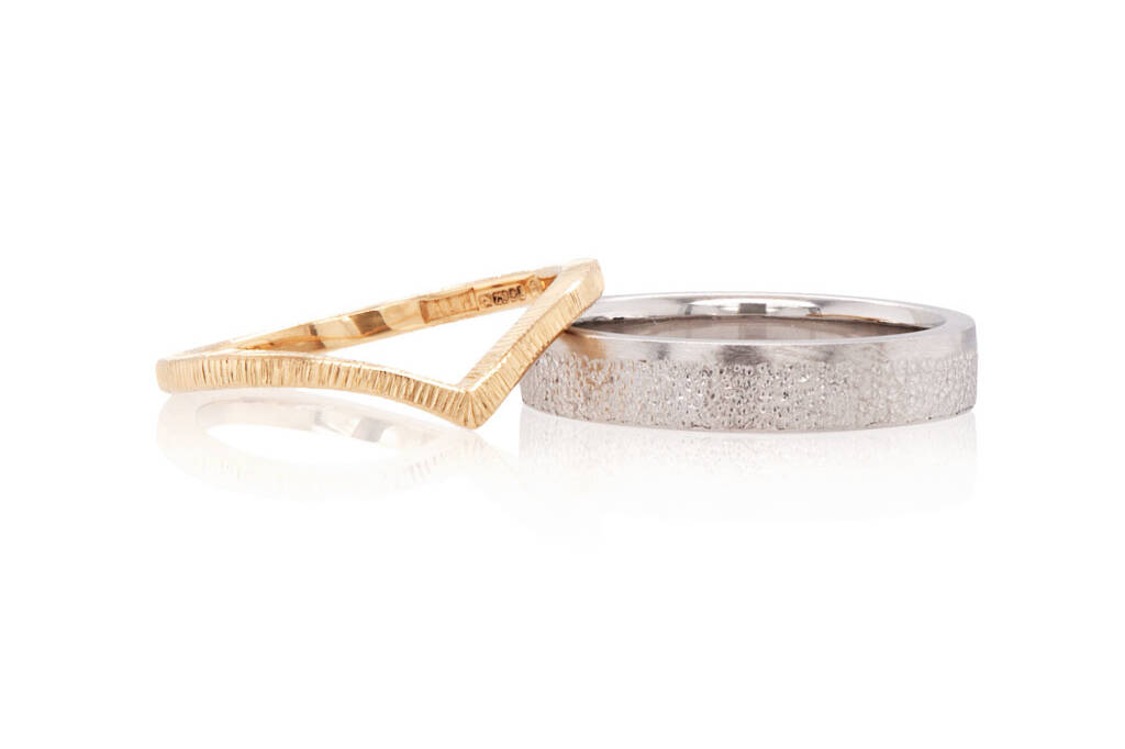 A gold wishbone and a platinum flat court ring on a white background. Both rings have hand applied finishes on the surfaces of each.