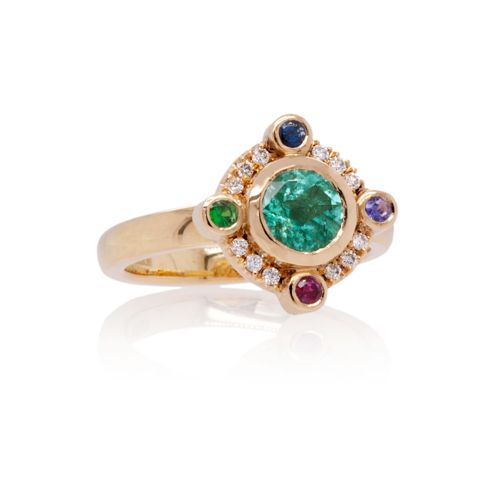 A round green-blue Paraiba tourmaline with 4 coloured gemstones set at the compass points around the around the tourmaline and small diamonds in between. The ring is made in 18k yellow gold and placed on a white background.