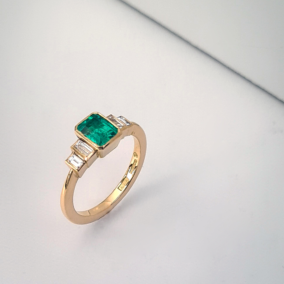 Emerald ring with two pairs of stepped baguette shoulders standing upright on a white background.