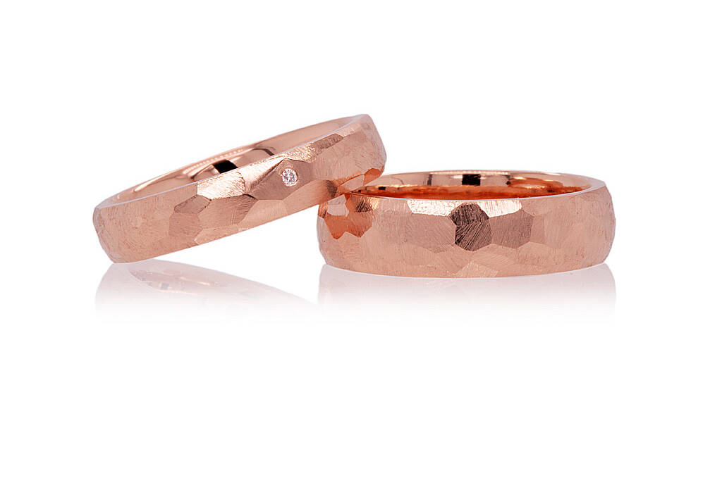 Red gold wedding rings with faceted finishes on a white background. One facet has a small diamond set flush inside.
