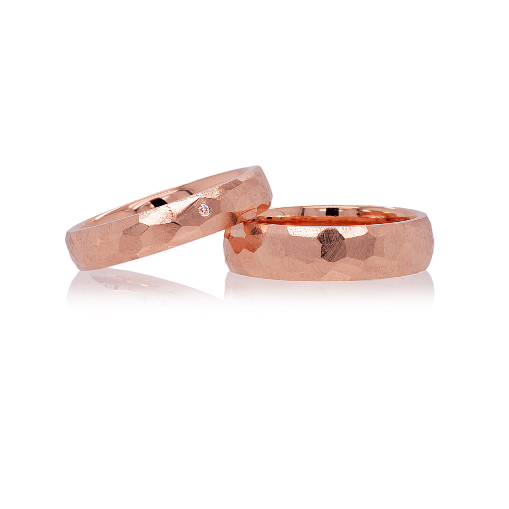 Red gold wedding rings with faceted finishes on a white background. One facet has a small diamond set flush inside.